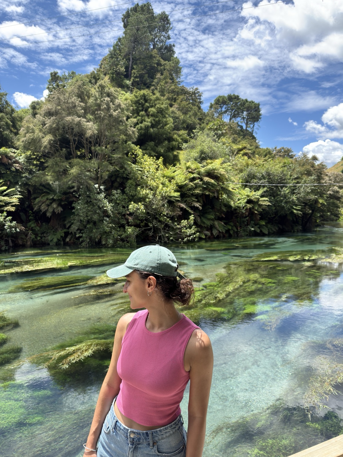 Fran de boné olhando as águas azul-turquesa do Blue Spring, na Nova Zelândia